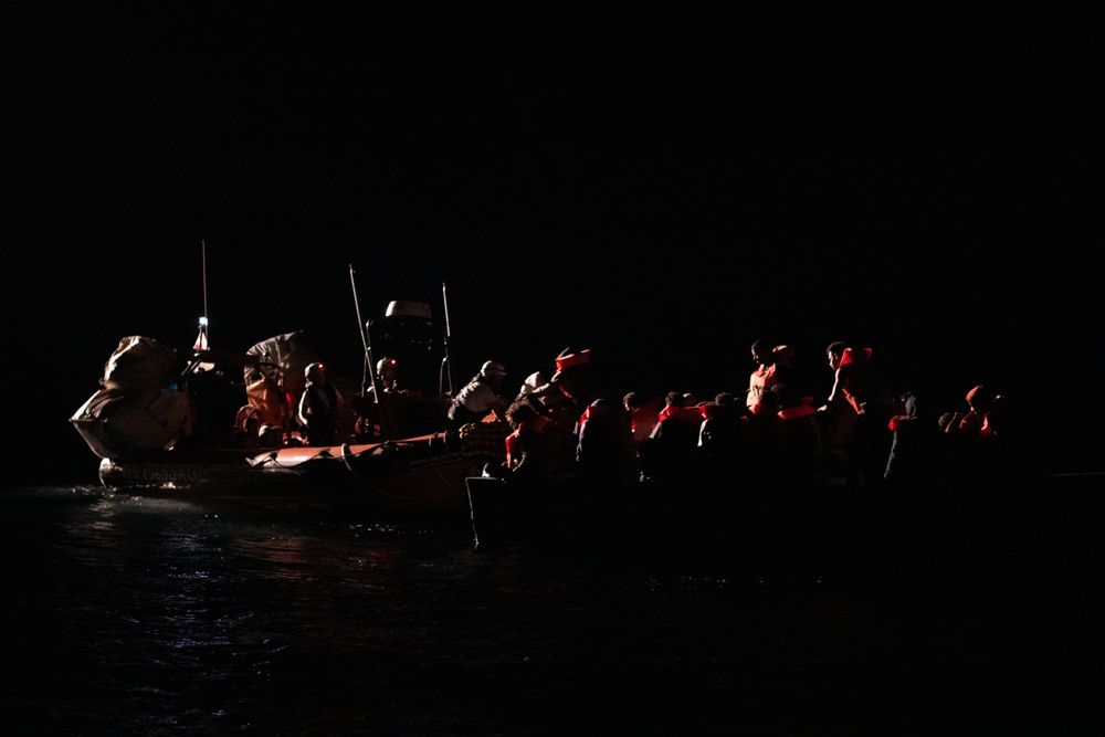 A team from the MSF search and rescue ship Geo Barents provides life vests to survivors on a wooden boat during a night-time rescue. © MICHELA RIZZOTTI/MSF