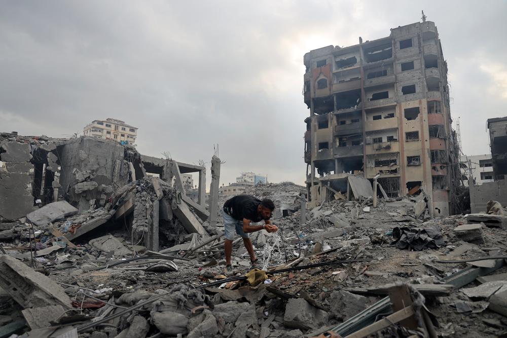 以色列與哈馬斯爆發衝突後，多棟樓房遭摧毀，圖中男子飲用爆裂水管中的食水。© MOHAMMED BABA