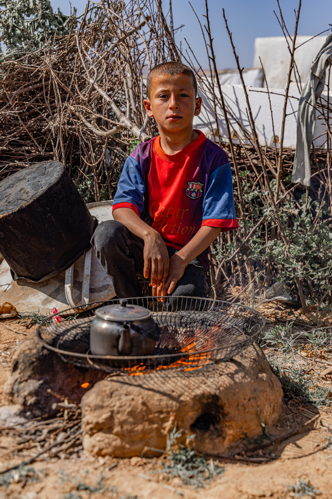 A Syrian child sits in front of a tea kettle on an open fire outside the tent he calls home. © Carmen Yahchouchi for MSF