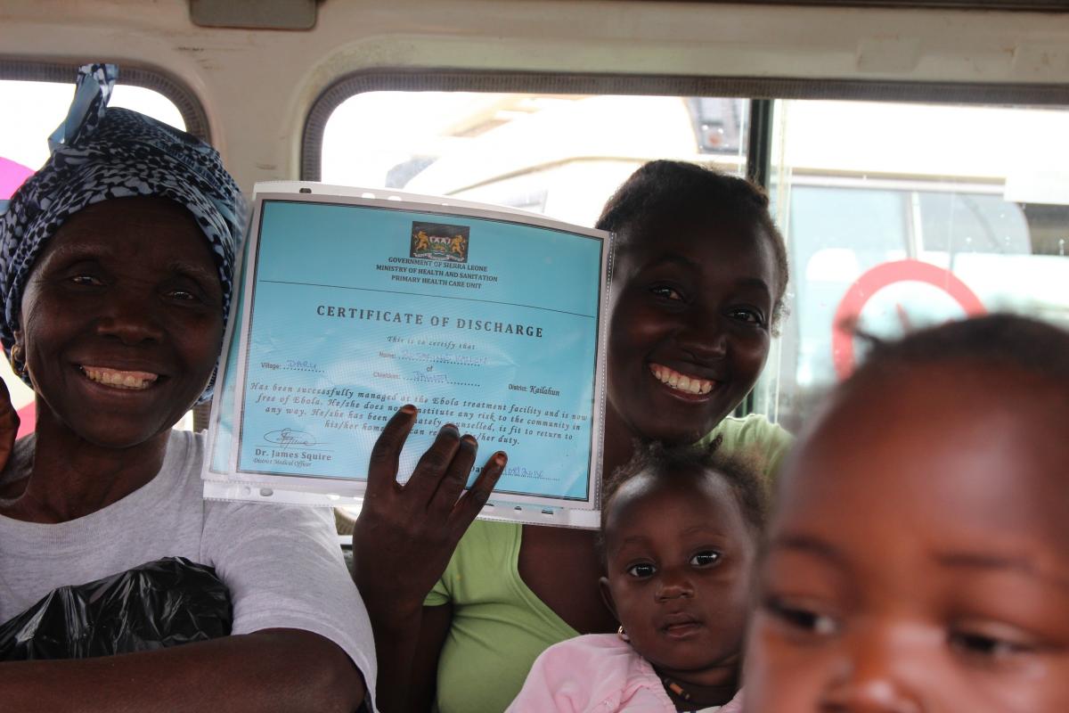 70歲的阿美、雅圖和兩歲大的女兒羅莎琳都是塞拉利昂的伊波拉康復者，他們高興地展示出院證書。無國界醫生的健康宣傳人員會陪同每一位康復者返家，向其家人和村民解釋他們已完全康復，不帶伊波拉病毒，不會對社群構成危險，可過正常生活。© P.K. Lee/MSF